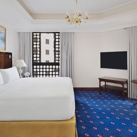 ダー アル ヒジラ インターコンチネンタル マディーナ エクステリア 写真 The photo shows an elegant hotel room. It features a large bed with a white comforter, wooden furniture, and a television mounted on the wall. There are decorative windows with intricate designs that allow natural light to filter in. The floor is cov