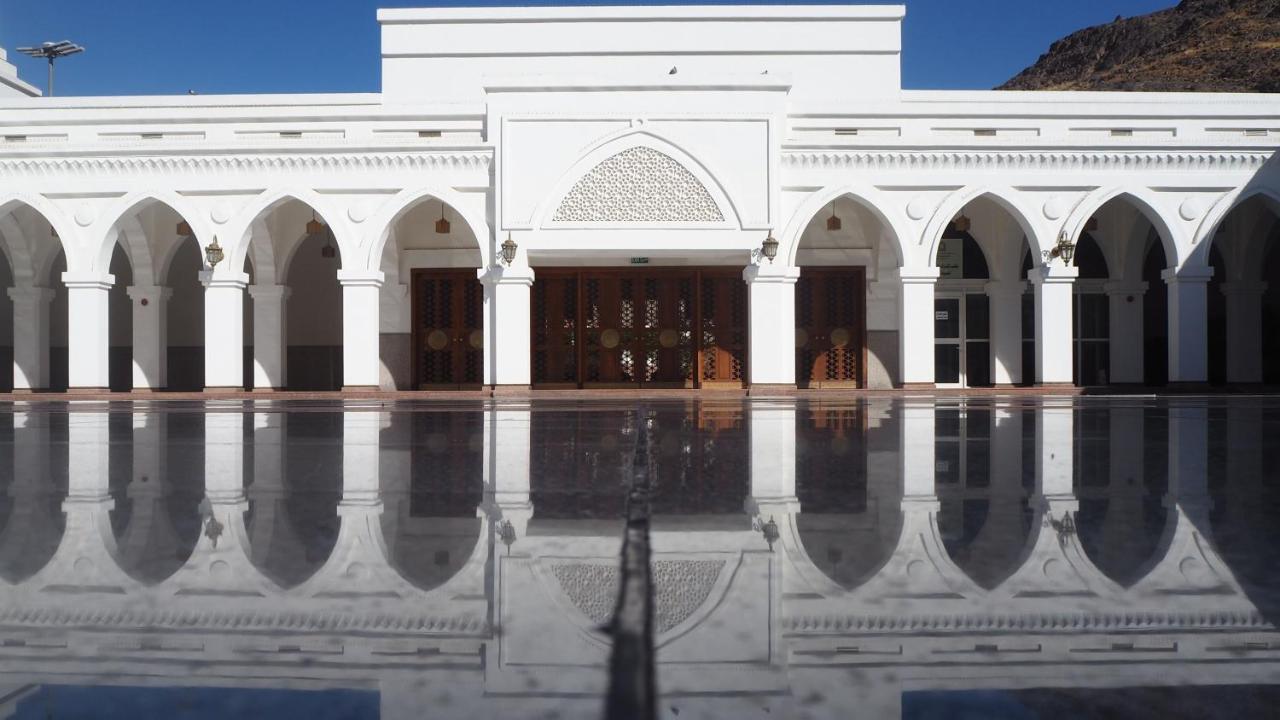 ダー アル ヒジラ インターコンチネンタル マディーナ エクステリア 写真 The photo shows a stunning white building with a symmetrical facade. It features several arched doorways and windows, which are typical of Islamic architectural design. The surface in front appears to be a smooth, reflective material, likely water or